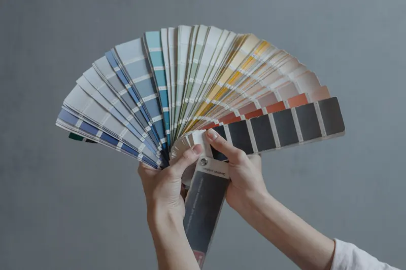 Unes mans sostenen un ventall de mostres de color davant d'una paret grisa.